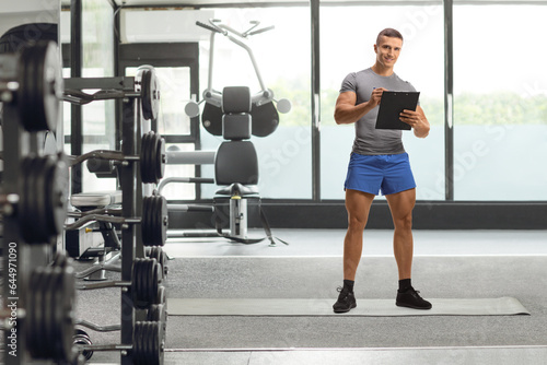 Full length portrait of a fitness instructor writing a document in a gym
