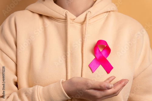 anonymous brazilian woman showing pink ribbon in beige background. breast cancer, awareness concept.