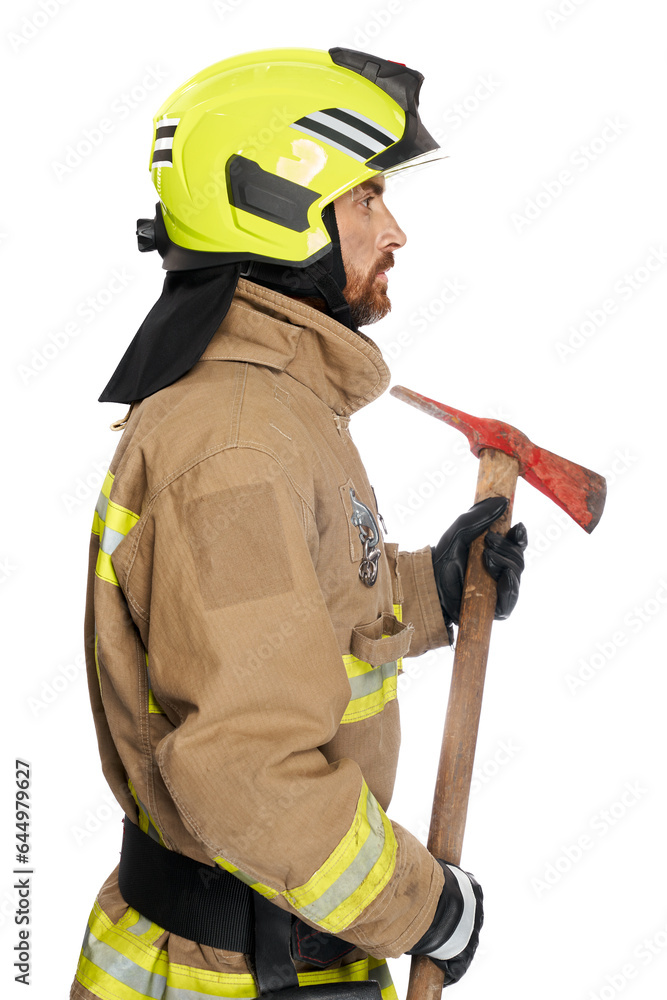 Focused male fireman using wooden axe tool for work. Side view of middle-aged man in fire uniform with hatchet looking away, isolated on white studio background. Job, equipment, tool concept. Focused male fireman using wooden axe tool for work. Side view of middle-aged man in fire uniform with hatchet looking away, isolated on white studio background. Job, equipment, tool concept.