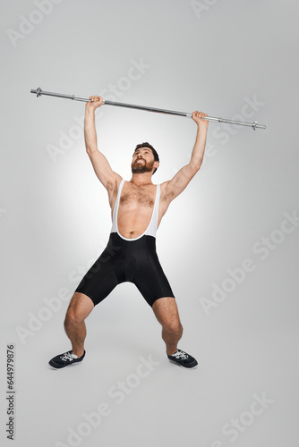 Muscular man in sportswear lifting unweighted barbell in studio. Full length of male powerlifter with clasped teeth exercising, isolated on white background. Concept of weightlifting, sport activity.