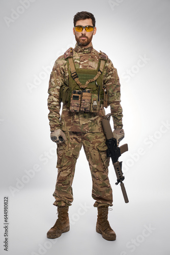 Fotografía Serious male soldier in body armor holding rifle, while posing indoors