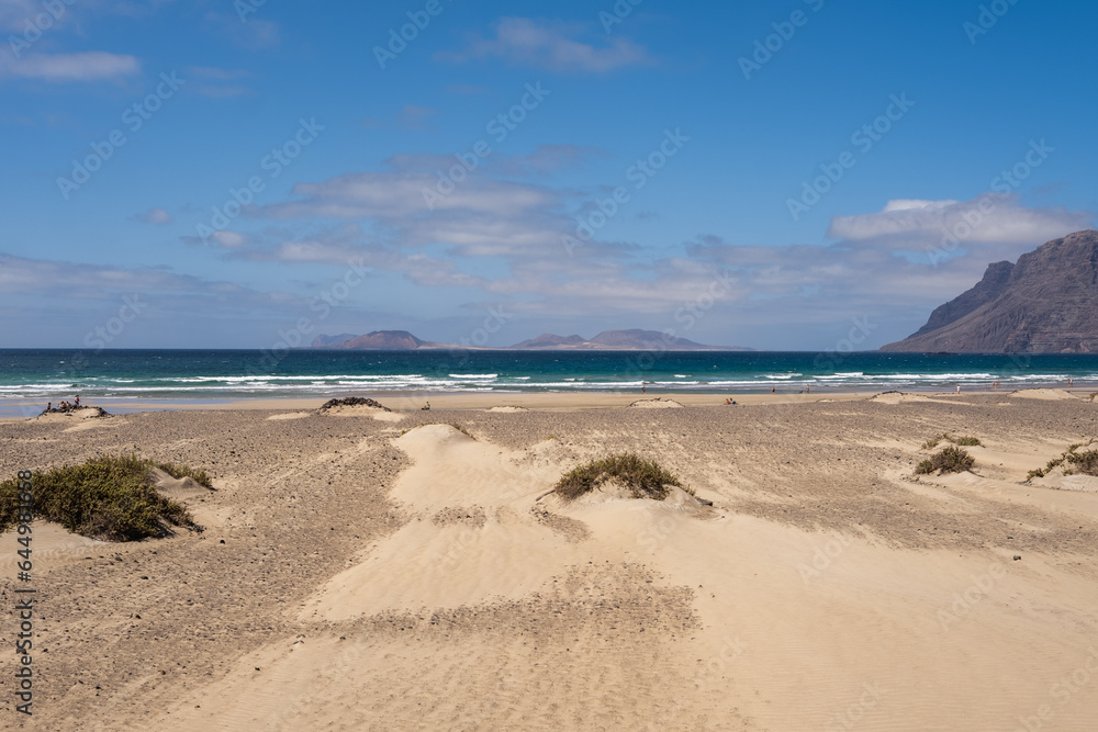 White sand beach. Famara beach. Turquoise water, island of La Graciosa and cliffs in the background. Sky with big white clouds. Caleta de Famara.Lanzarote, Canary Islands, Spain.