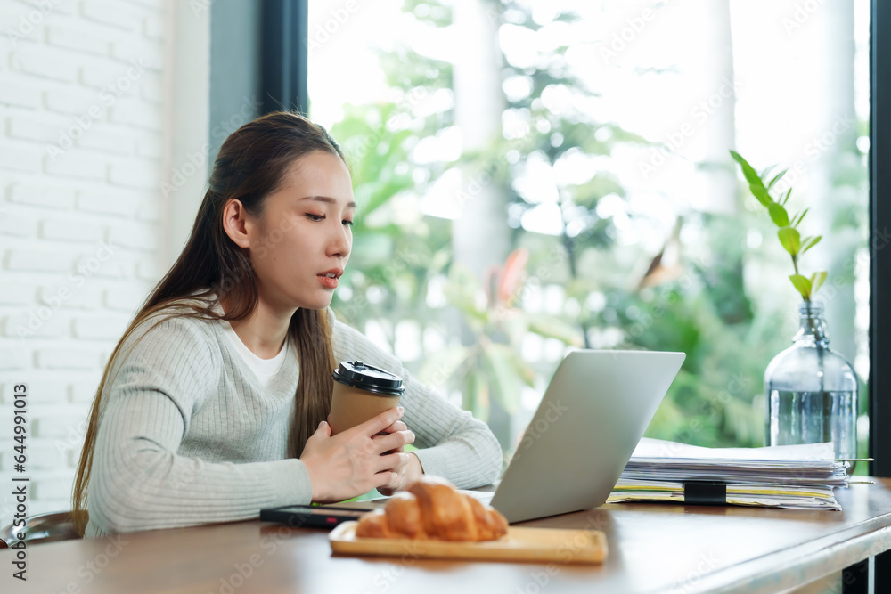 Asian woman with tired face editing work on vacation to relax There is coffee on the table, drinks, snacks, documents, a hand on a coffee cup symbolizes boredom. Asian woman with tired face editing work on vacation to relax There is coffee on the table, drinks, snacks, documents, a hand on a coffee cup symbolizes boredom.