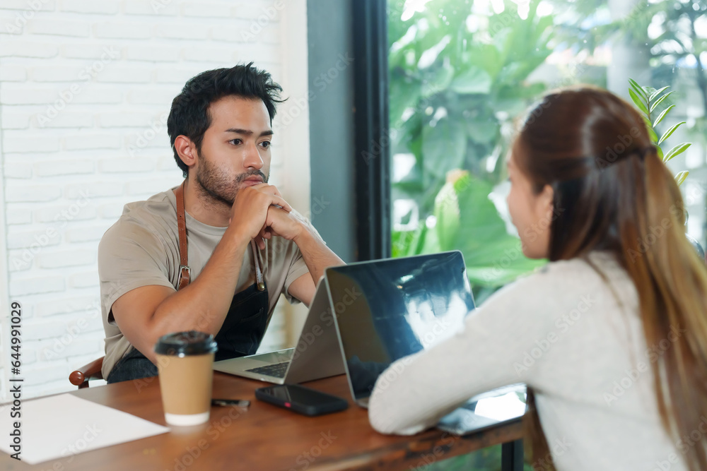 Asian man sitting on chin showing boredom in front of laptop computer Between accounting income and expenses of a small family business, a coffee shop, and calling his wife to watch the screen. Asian man sitting on chin showing boredom in front of laptop computer Between accounting income and expenses of a small family business, a coffee shop, and calling his wife to watch the screen.