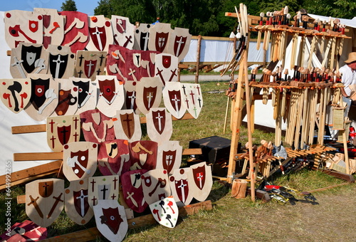 A close up on a stall full of swords, shields, targes, arrows, bows, axes, and other medieval weaponry made out of metal and wood displayed for sale during a medieval fair or festival in Poland