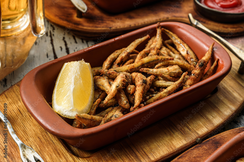 Tasty fried anchovies in cornmeal with lemon piece in wooden background, grilled small fish for beer, snacks