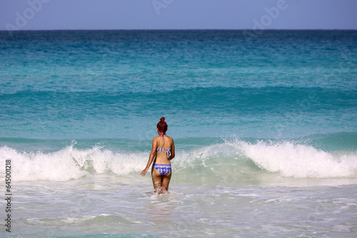 Girl in swimsuit going to swim in azure sea water. Beach vacation on sunny coast