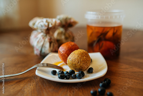 Soft cheese balls adorned with blueberries and paprika, artfully arranged on a white plate atop a rustic wooden table. Delightful culinary composition.