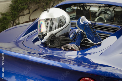 A lifestyle shot of a British sports car with driving shoes, driving gloves, sunglasses, and a racing helmet arranged on the engine cover