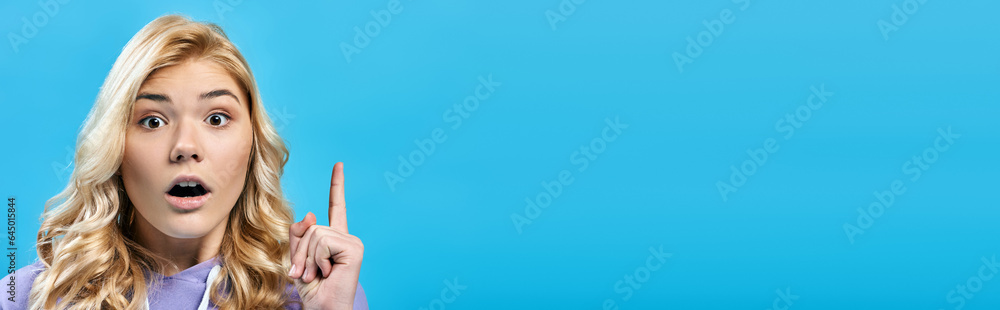 excited blonde teenage girl with open mouth showing idea sign on blue and looking at camera, banner excited blonde teenage girl with open mouth showing idea sign on blue and looking at camera, banner