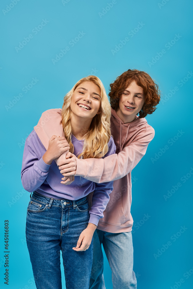 redhead teen guy embracing laughing girlfriend on blue, friendship of stylish teenagers redhead teen guy embracing laughing girlfriend on blue, friendship of stylish teenagers