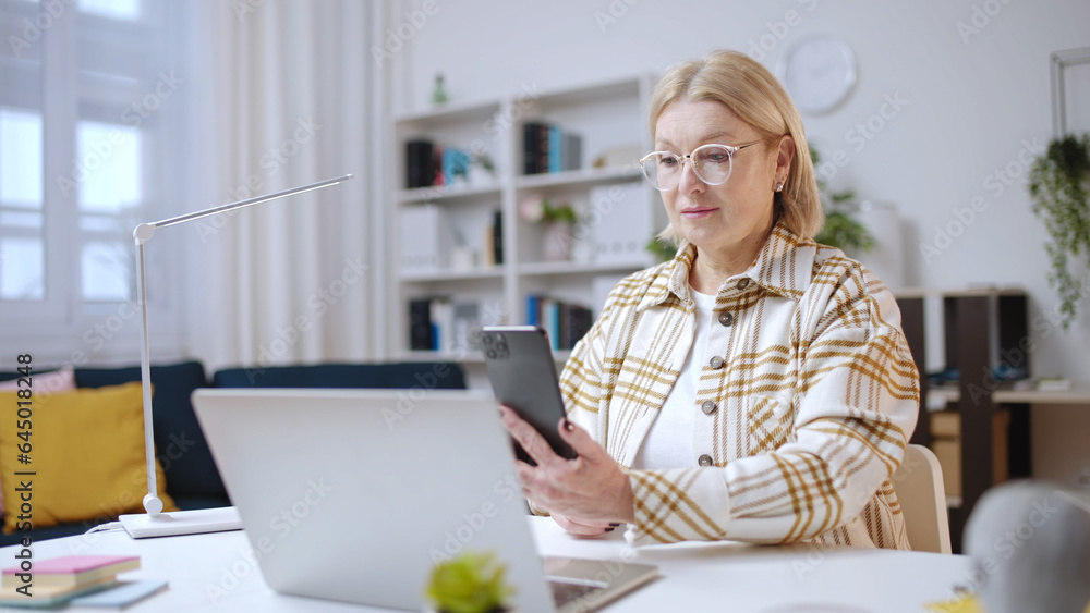 Woman in her 50s using smartphone to make a purchase, scanning qr code on laptop Woman in her 50s using smartphone to make a purchase, scanning qr code on laptop