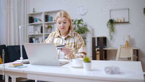 Mature woman entering credit card number, doing shopping online and ordering delivery