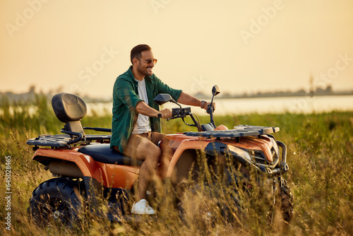 An excited man driving a rented quad bike and looking around the nature.