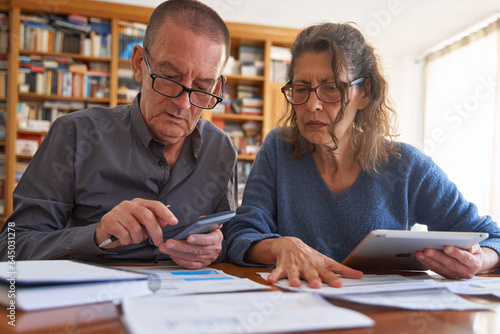 Senior male and senior female with tablet and calculator anxious while managing bills and paperwork. Couple doing omestic life budget