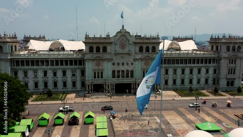 Bandera Guatemalteca ondenado al viento sobre asta en del centro de la capital de la ciudad con palacio nacional de cultura de fondo en Guatemala  photo