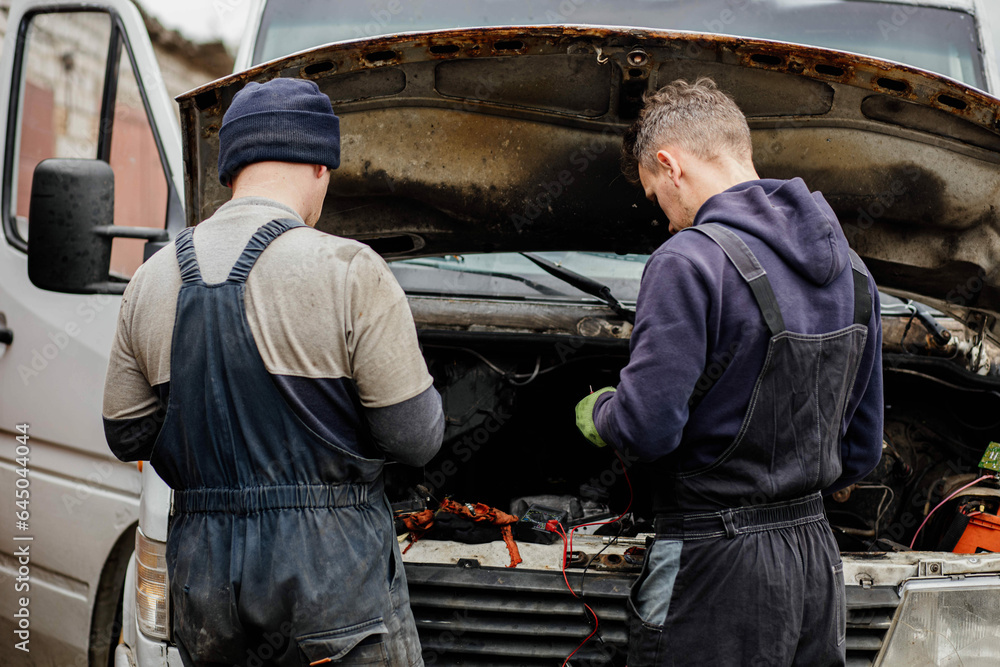 two master auto mechanics diagnosing a van with the hood raised two master auto mechanics diagnosing a van with the hood raised