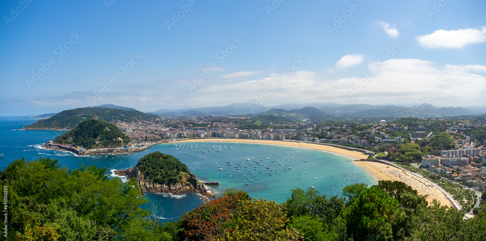 Panoramic view of La Concha beach in the basque city of San Sebastian with sailboats and blue sky. Summer vacation tourist destination seascape.