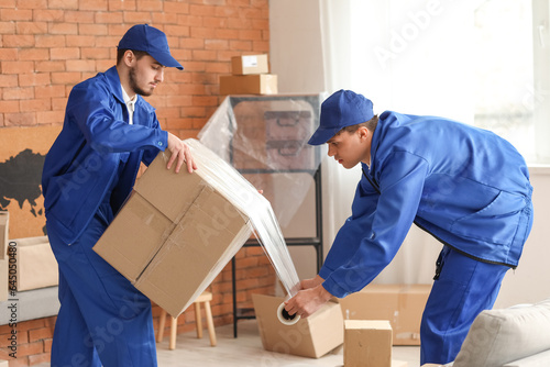 Quadro su tela Male movers wrapping box with stretch film in room