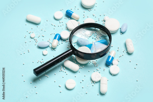 Magnifier with pills on blue background photo