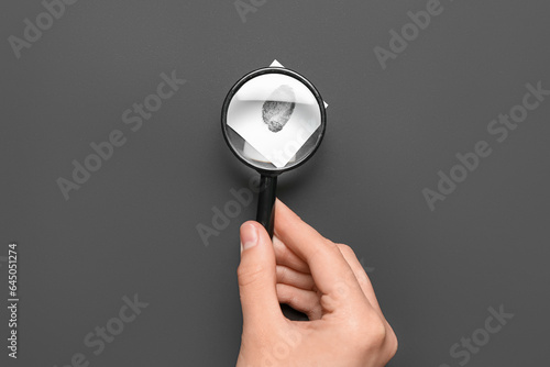 Female hand with magnifier and paper with fingerprint on black background. Detective concept photo