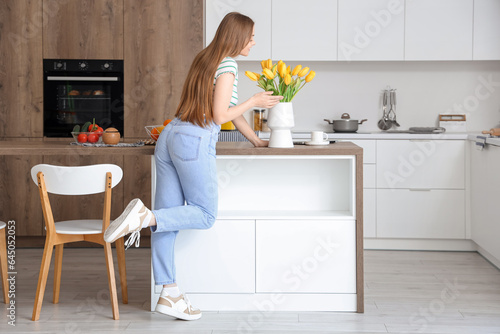 Beautiful young woman smelling blooming tulip flowers in modern kitchen