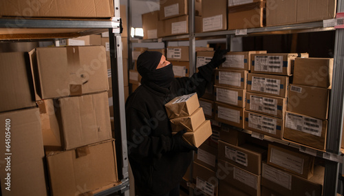 Thief wears gloves steal boxes of goods in a warehouse in the dark. Concept of problems with theft of postal parcels.