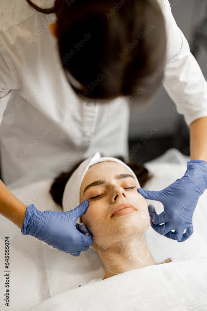 Young woman receiving cream on her face before beauty procedure at beauty salon, close-up view from above