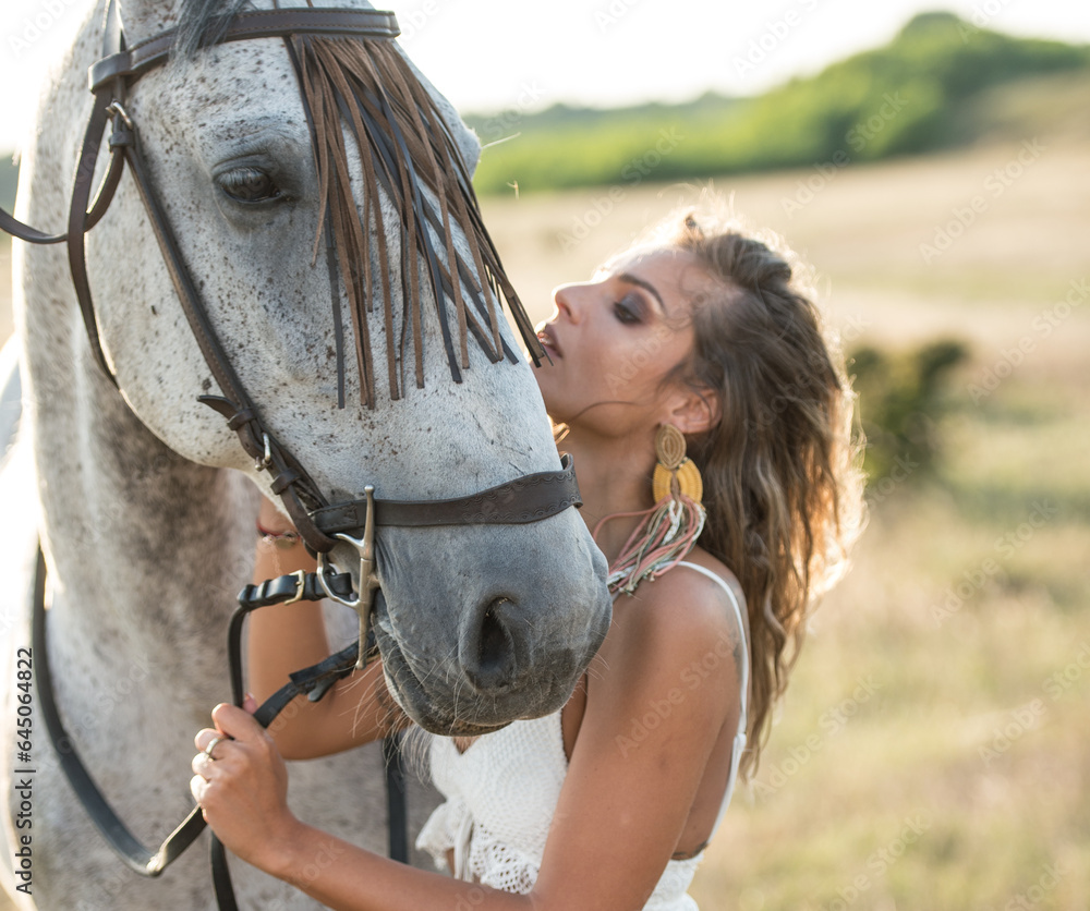 Beautiful blonde woman with curly hair with white hat and horse. Portrait of a girl with denim and her horse. Beautiful girl interacting and having fun with a horse at the ranch