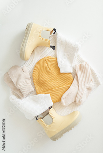 Set of baby sweater, hat, socks, gloves and rubber boots. Stylish children's clothes for spring, autumn or winter in white and yellow colors. Flat lay, top view