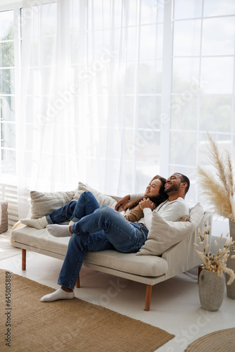 Joyful young multiethnic couple relaxing and cuddling on couch in living room 