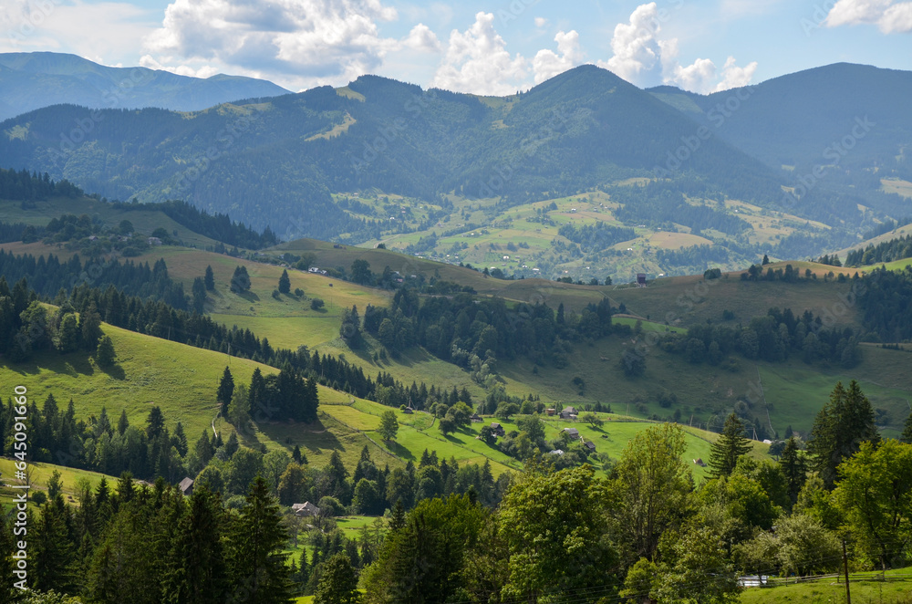 Mountain rural landscape with beautiful village on the hills covered grass and trees. Carpathian Mountains, Ukraine