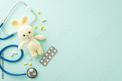 Kids\' wellness concept. Top view picture featuring stethoscope for medical check-ups, blister pack of pills, numerous scattered medications, bunny on light blue backdrop with empty area for text or ad
