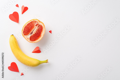 Understanding sexuality: top view shot of grapefruit half, symbolizing female genital, banana, evoking male anatomy, and hearts, set against white backdrop, providing space for text or promo content