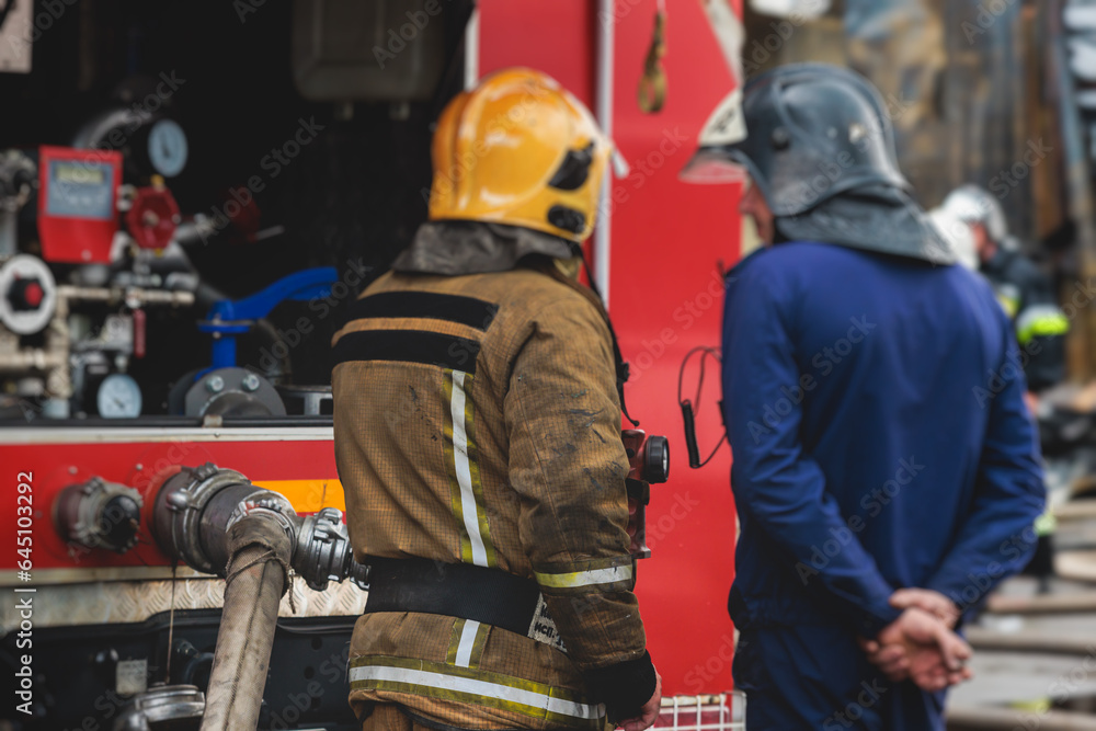 Group of fire men in protective uniform during fire fighting operation in the city streets, firefighters brigade with the fire engine truck vehicle in the background, emergency and rescue service Group of fire men in protective uniform during fire fighting operation in the city streets, firefighters brigade with the fire engine truck vehicle in the background, emergency and rescue service