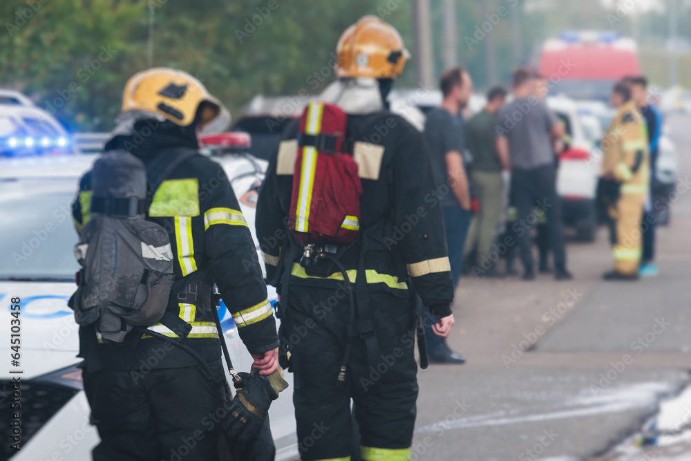 Group of fire men in protective uniform during fire fighting operation in the city streets, firefighters brigade with the fire engine truck vehicle in the background, emergency and rescue service Group of fire men in protective uniform during fire fighting operation in the city streets, firefighters brigade with the fire engine truck vehicle in the background, emergency and rescue service