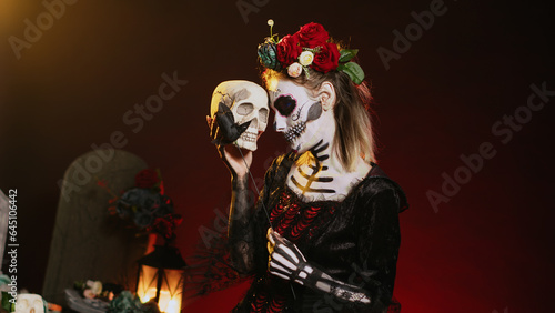 Glamorous woman acting creepy with skull in hand, holding black roses and wearing scary make up. Looking like santa muerte with body art on holy mexican celebration, being flirty. Handheld shot.