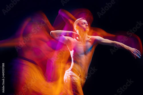 Chaotic movements. Young muscular shirtless man in motion against black studio background in neon with mixed lights effect. Concept of movements, art, dance and sport, fashion, youth, ad