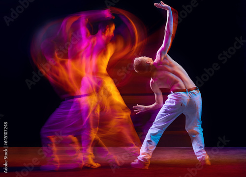Fototapeta Naklejka Na Ścianę i Meble -  Inspiration and freedom. Young shirtless guy making chaotic movements against black studio background in neon with mixed lights effect. Concept of movements, art, dance and sport, fashion, youth, ad