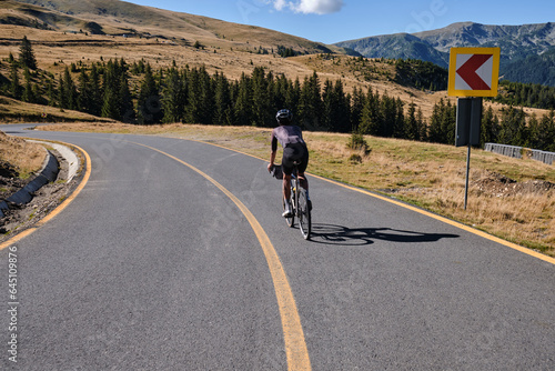 Male cyclist wearing black cycling kit and helmet, is training on a gravel bike in the mountains, enjoying an amazing view. Man cyclist is riding downhill on the Transalpina road.Parâng Mountains