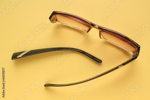 Old broken eyeglasses with damaged legs on orange background. Poor eyesight. Reuse and repair concept. Idea of health. Failure optic eyewear. Breakage of vision correction glasses. Close up, flat lay