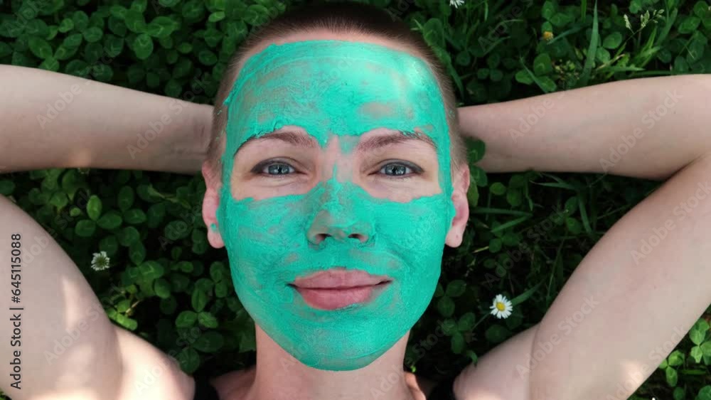 Woman with green cosmetic mask on her face is lying on grass. Woman with green cosmetic mask on her face is lying on grass.
