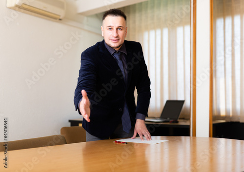 Positive European man office manager reaching out his hand for handshake and looking in camera. High quality photo