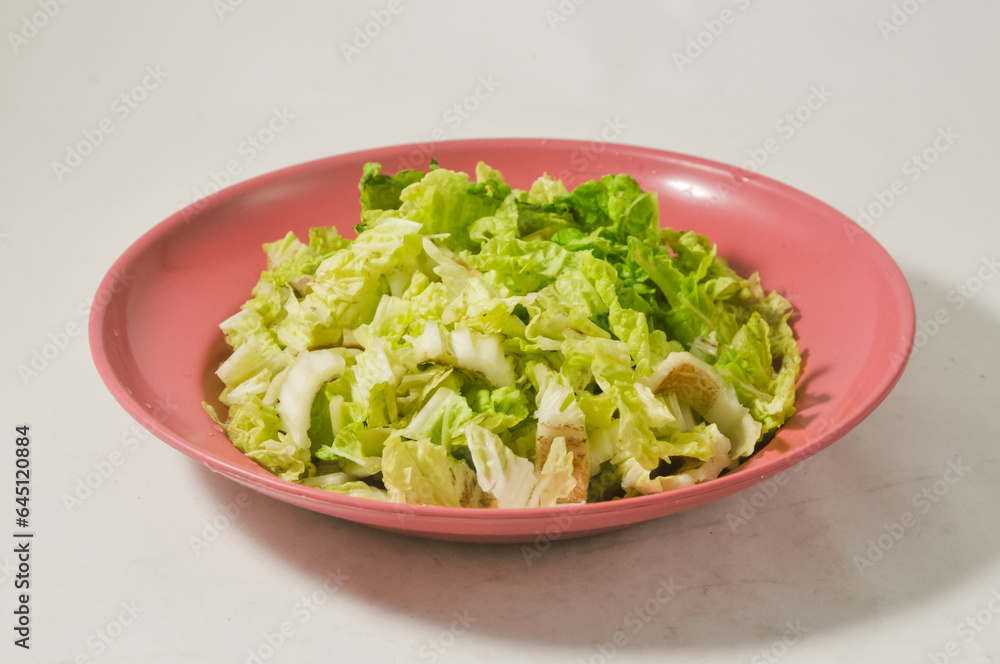 Chopped Chinese cabbage in a red plastic plate on a wooden cutting board isolated on a white background