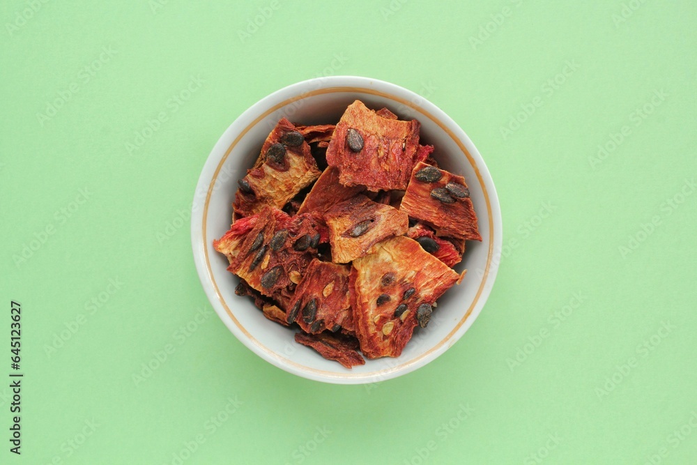 Slices of red dehydrated watermelon pulp pieces at white bowl on green background. Dried fruit chips. Organic natural healthy snack food. Homemade vegan diet. Home cooked superfood dessert Slices of red dehydrated watermelon pulp pieces at white bowl on green background. Dried fruit chips. Organic natural healthy snack food. Homemade vegan diet. Home cooked superfood dessert