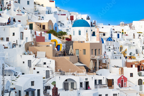 Santorini, Greece - 05 27 2023: Oia caldera's colorful white-washed terraces with blue domes on a bright morning