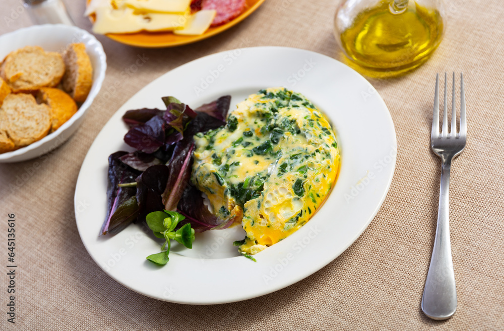 Appetizing omelette with spinach served on dish in restaurant