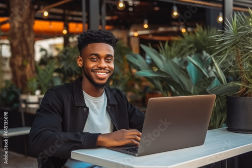 Handsome smiley young male african american office assistant working remotely on her computer outside the coffee shop