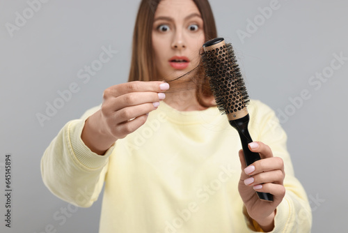 Woman untangling her lost hair from brush on light grey background, selective focus. Alopecia problem