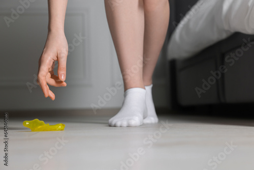 Woman taking unrolled condom from floor indoors, closeup. Safe sex